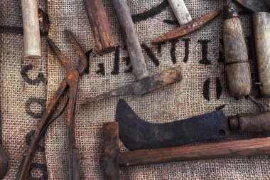 Eski zanaatkar araçları arka planda, bir çiftçinin bir çuvala taktığı klasik eşyalar.