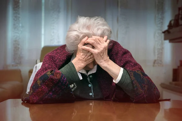 Loneliness of old woman. Senior lady sitting on the chair with her hands covering the face (unrecognizable person)