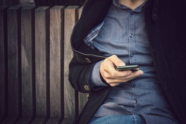 Akıllı telefon kullanan bir adama yakın çekim, sıradan bir erkek bankta oturuyor ve cep telefonunda yazıyor.