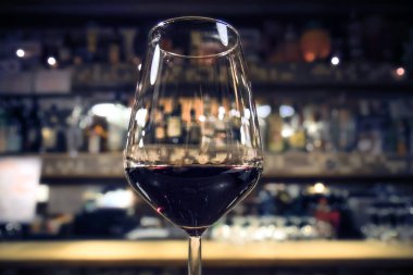 Bir barda kırmızı şarap, arka planda bulanık alkol şişeleri olan bağımlılık konsepti (soğuk ton)