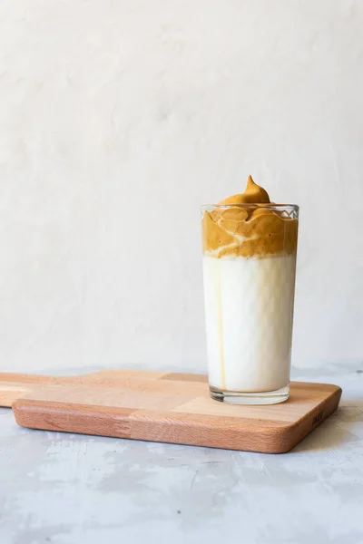 Glass of coffee dalgon on a wooden board. Light gray concrete background. Trendy drink from Korea.