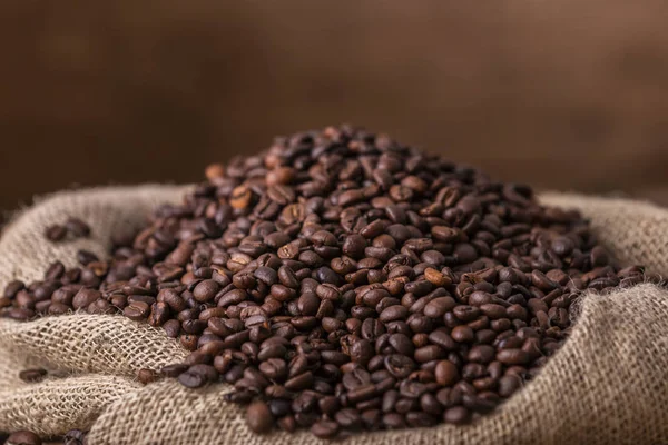 在棕色木质背景上洒满新鲜咖啡豆的麻袋 — 图库照片