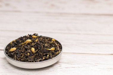 Beyaz tahta masada Yasemin çiçekleri küçük tabak içinde parçacıkların kuru kahverengi çay görünümünü yakın çekim yaprak