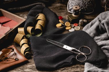 Kompozisyon makas, dikiş makaralar, mezura ve gözlüklü renkli düğmeler siyah polka noktalı kumaş üzerinde kaba ahşap masa yerleştirilir