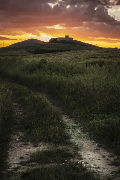 美丽的 Unsurfaced 轨道领导上山到老石堡垒与绿色草周围与明亮的橙色多云日落天空在夏天背景 — 图库照片