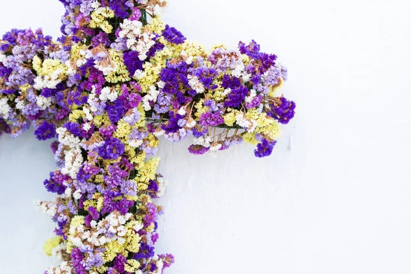 白い漆喰壁に掛かっている小さな色とりどりの花で飾られた素晴らしいクロス — ストック写真