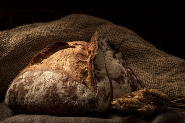 Büyük kahverengi pişmiş somun ekmek kanvas malzeme üzerinde koyu arka plan üzerinde buğday ile