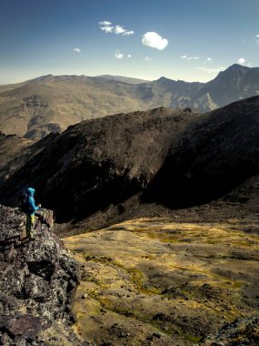 Sırt çantası uçurumda duran ve güneşli bir günde muhteşem dağlara bakan tanınmayan yürüyüşçü yan görünümü