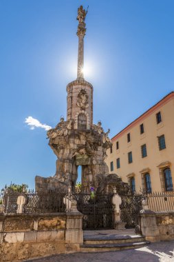 From below show of San Rafael Arcangel column with statue on top placed behind fence under blue sky in Cordoba, Spain