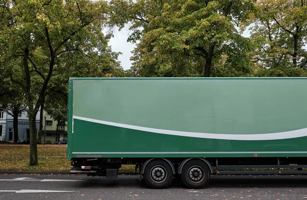Vista lateral de um trailer verde com espaço em branco para gráficos em uma estrada com árvores verdes — Fotografia de Stock