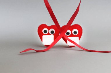 Maskeli ve gözlü kırmızı kalpler bir kurdele ile kaplıdır. Kopyalama alanı - sosyal mesafe kavramı, önleme, karantina, güvenlik, koronavirüsün yayılması, yasaklama.