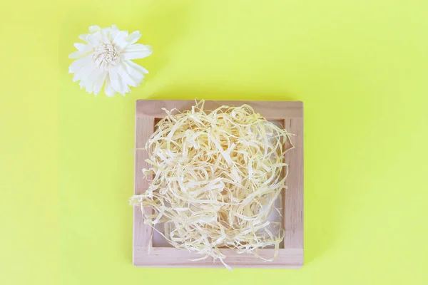 Cardboard, organic box filled with shredded paper on a yellow background top view. Holiday card. Copy space - concept of environmental packaging for gifts for a birthday, wedding, mothers day