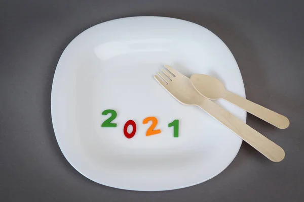 Multicolored wooden numbers 2021 near a white plate. Defocused fork and spoon on a gray background. Copy space - concept new year 2021, coronavirus, crisis, economy, food, hunger, unemployment — Stock Photo, Image