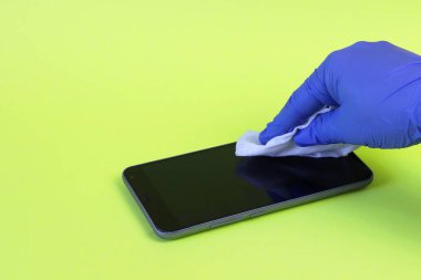 Elinde dezenfektan peçeteyle bir eldivenin içindeki el akıllı telefonun yüzeyindeki kiri siliyor. Kopyalama alanı - temizlik ekipmanları, temizlik, koronavirüs yayılması, önleme.