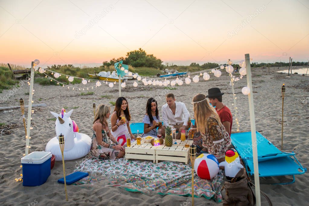 Group of friends having a picnic at the beach - Happy young people on a summer vacation at the beach
