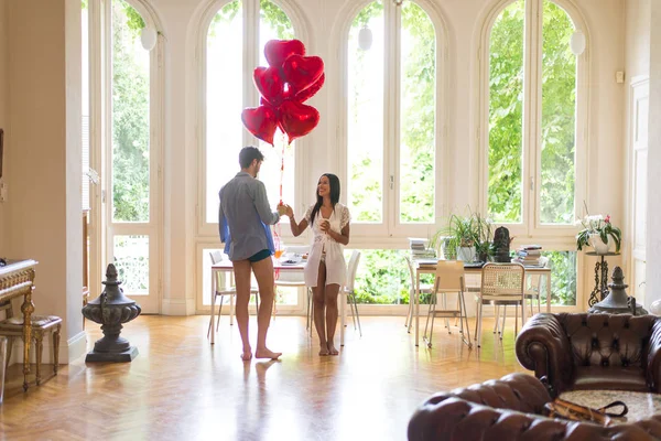 Romantic moments at home, boyfriend presenting heart shaped balloons to his girlfriend