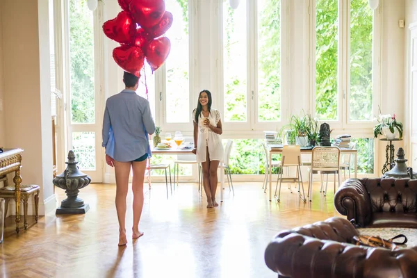 Romantic moments at home, boyfriend presenting heart shaped balloons to his girlfriend