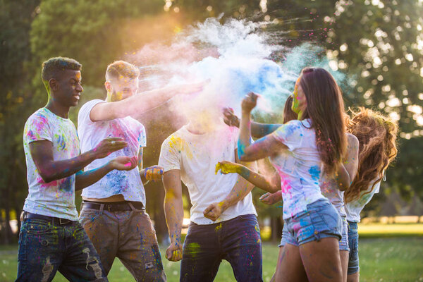 Группа счастливых друзей, играющих цветами цвета холи в парке - Молодые люди веселятся на фестивале холи, концепция веселья, веселья и молодого поколения
