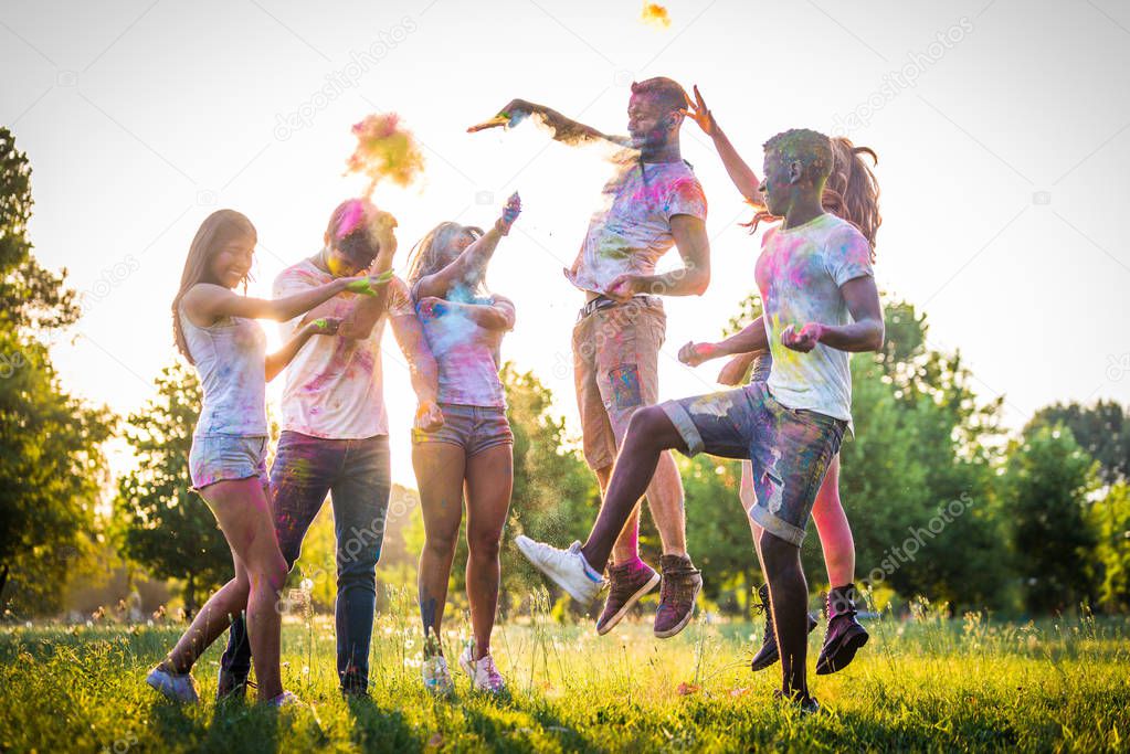 Group of happy friends playing with holi colors in a park - Young adults having fun at a holi festival, concepts about fun, fun and young generation