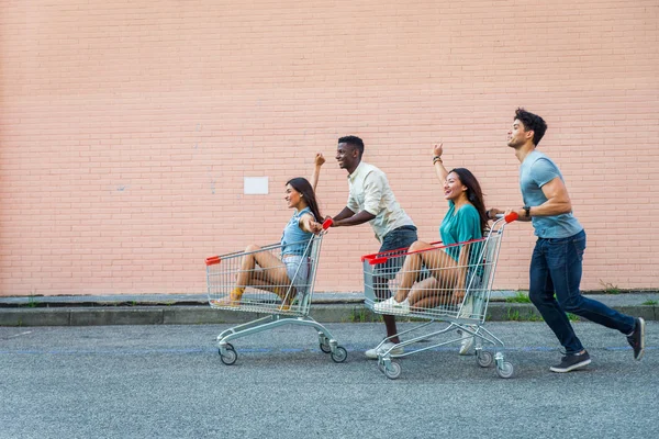 駐車場でショッピングカートで遊んで友達の多民族のグループ — ストック写真