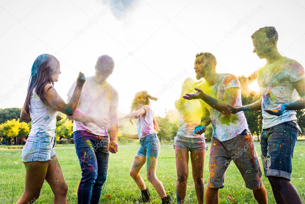 Group of happy friends playing with holi colors in a park - Young adults having fun at a holi festival, concepts about fun, fun and young generation