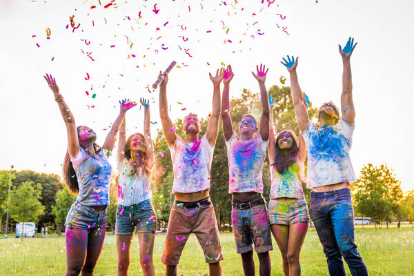 Group of happy friends playing with holi colors in a park - Young adults having fun at a holi festival, concepts about fun, fun and young generation