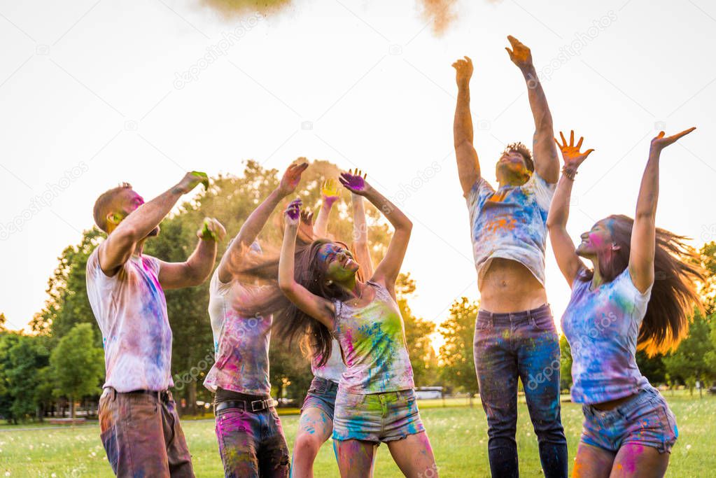 Group of happy friends playing with holi colors in a park - Young adults having fun at a holi festival, concepts about fun, fun and young generation