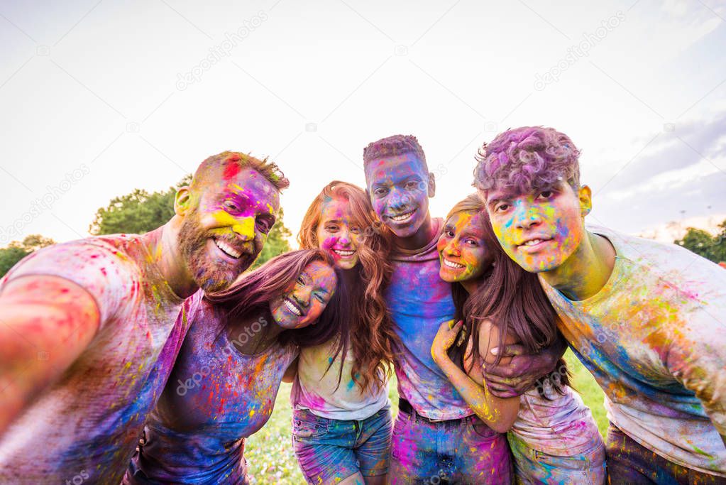 Group of happy friends playing with holi colors in a park - Young adults having fun at a holi festival, concepts about fun, fun and young generation