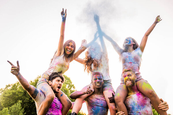 Group of happy friends playing with holi colors in a park - Young adults having fun at a holi festival, concepts about fun, fun and young generation