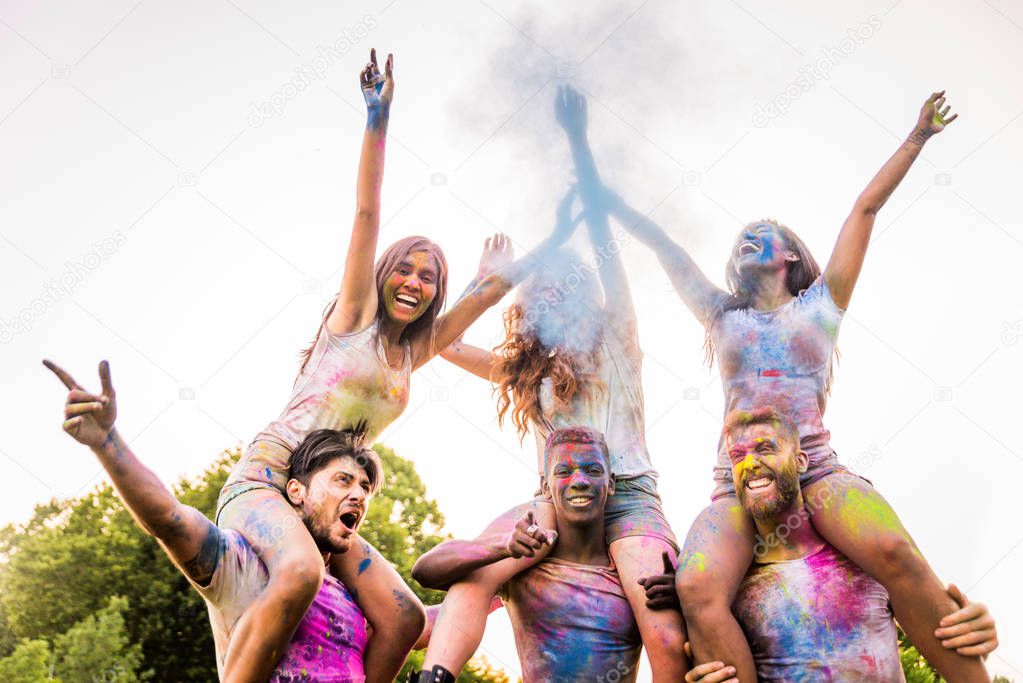 Group of happy friends playing with holi colors in a park - Young adults having fun at a holi festival, concepts about fun, fun and young generation