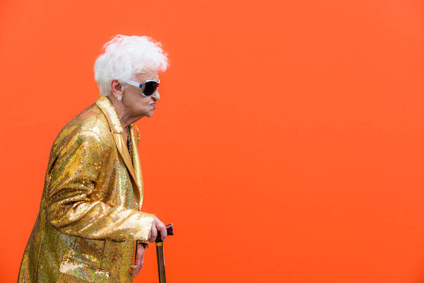 Смешная и экстравагантная пожилая женщина позирует на цветном фоне - молодая старушка в шестидесятых веселится и веселится
