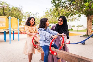 Dubai - anne ile birlikte kızları park oyun alanındaki eğleniyor mutlu Arap aile