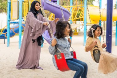 Dubai - anne ile birlikte kızları park oyun alanındaki eğleniyor mutlu Arap aile