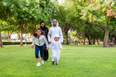 Dubai - ebeveynler ve çocuklar hafta sonu doğada kutluyor bir parkta eğleniyor mutlu bir Orta Doğulu aile