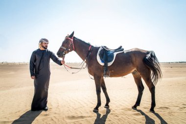 Yakışıklı adamla Orta Doğu: Dubai çölünde Arapça bir binicilik tipik Emirlikleri elbise