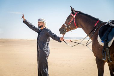 Yakışıklı adamla Orta Doğu: Dubai çölünde Arapça bir binicilik tipik Emirlikleri elbise