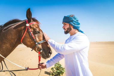 Yakışıklı adamla Orta Doğu: Dubai çölünde Arapça bir binicilik tipik Emirlikleri elbise