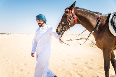 Yakışıklı adamla Orta Doğu: Dubai çölünde Arapça bir binicilik tipik Emirlikleri elbise
