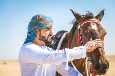Yakışıklı adamla Orta Doğu: Dubai çölünde Arapça bir binicilik tipik Emirlikleri elbise