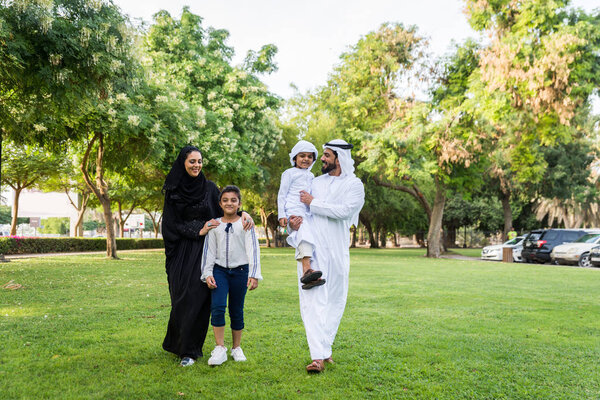 Happy middle-eastern family having fun in a park in Dubai - Parents and kids celebrating the weekend in the nature