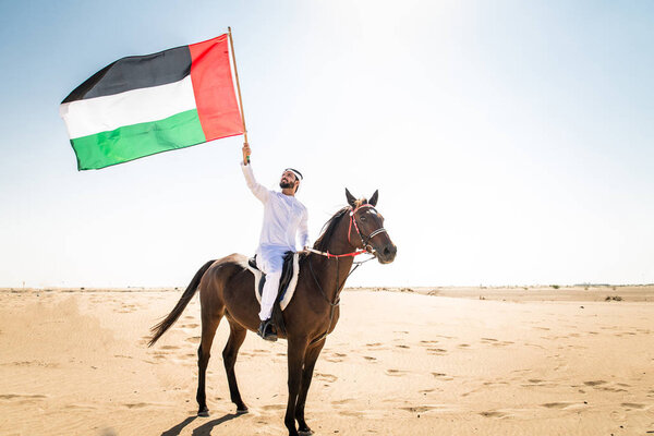 Middle eastern handsome man with typical emirates dress riding a arabic horse in the Dubai desert