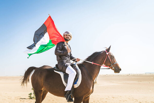 Middle eastern handsome man with typical emirates dress riding a arabic horse in the Dubai desert