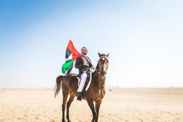 Middle eastern handsome man with typical emirates dress riding a arabic horse in the Dubai desert