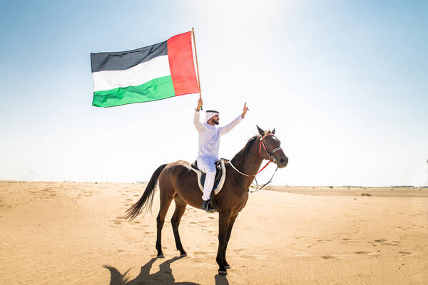 Middle eastern handsome man with typical emirates dress riding a arabic horse in the Dubai desert