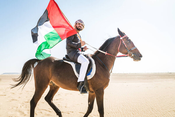 Middle eastern handsome man with typical emirates dress riding a arabic horse in the Dubai desert