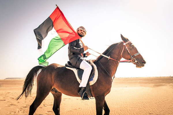 Middle eastern handsome man with typical emirates dress riding a arabic horse in the Dubai desert