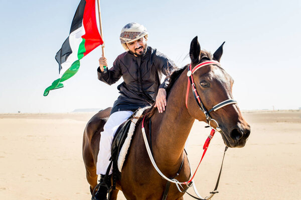 Middle eastern handsome man with typical emirates dress riding a arabic horse in the Dubai desert