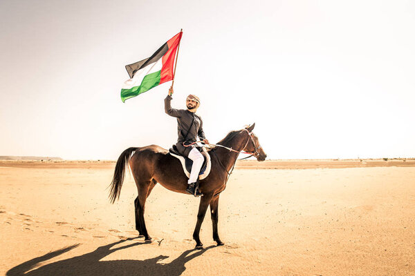 Middle eastern handsome man with typical emirates dress riding a arabic horse in the Dubai desert