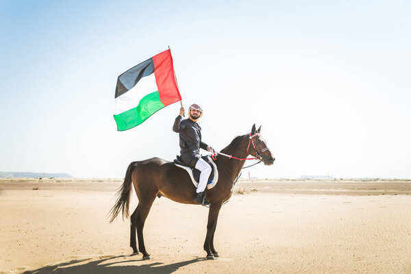 Middle eastern handsome man with typical emirates dress riding a arabic horse in the Dubai desert