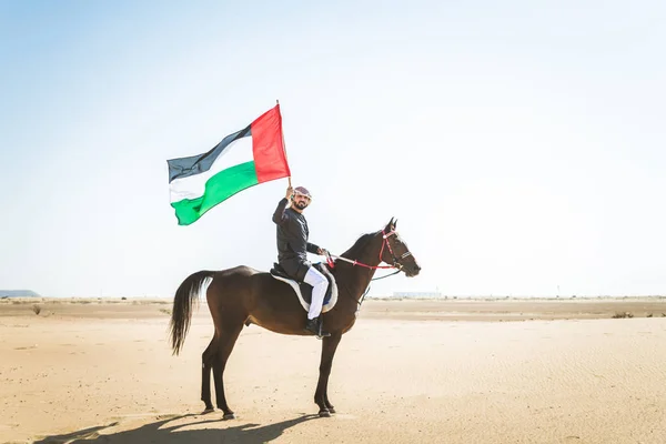 Middle eastern handsome man with typical emirates dress riding a arabic horse in the Dubai desert